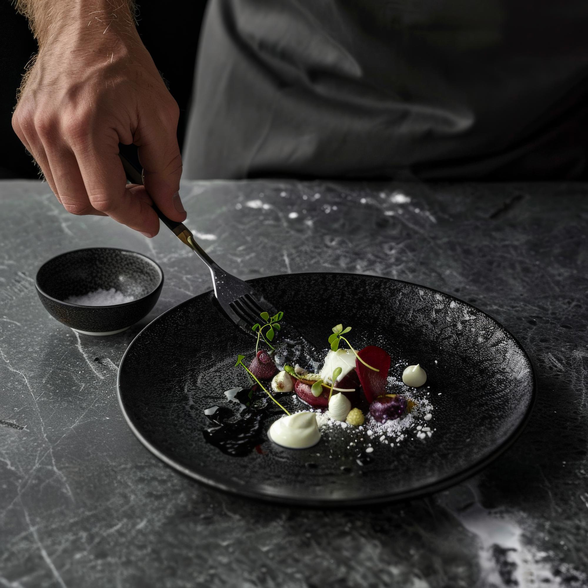 Chef plating a refined dish on dark table